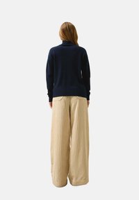 Maglione a dolcevita blu marino abbinato a larghi pantaloni beige plissettati, con righe verticali e vestibilità rilassata.