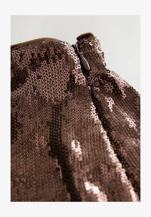 Close-up of brown sequined fabric with a brown zipper pull tab on a garment against a light background.