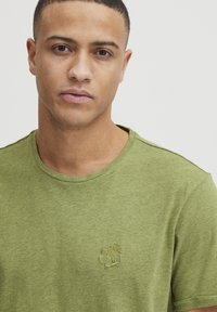 Grøn bomulds t-shirt med rund halsudskæring og korte ærmer. Har en diskret palmetræ broderi på brystet, let og tekstureret.