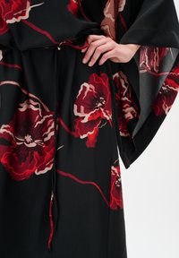 Rochie neagră cu un model floral format din flori mari roșii și bej, dintr-un material fluid cu o textură netedă, și o talie strânsă pentru a crea formă.