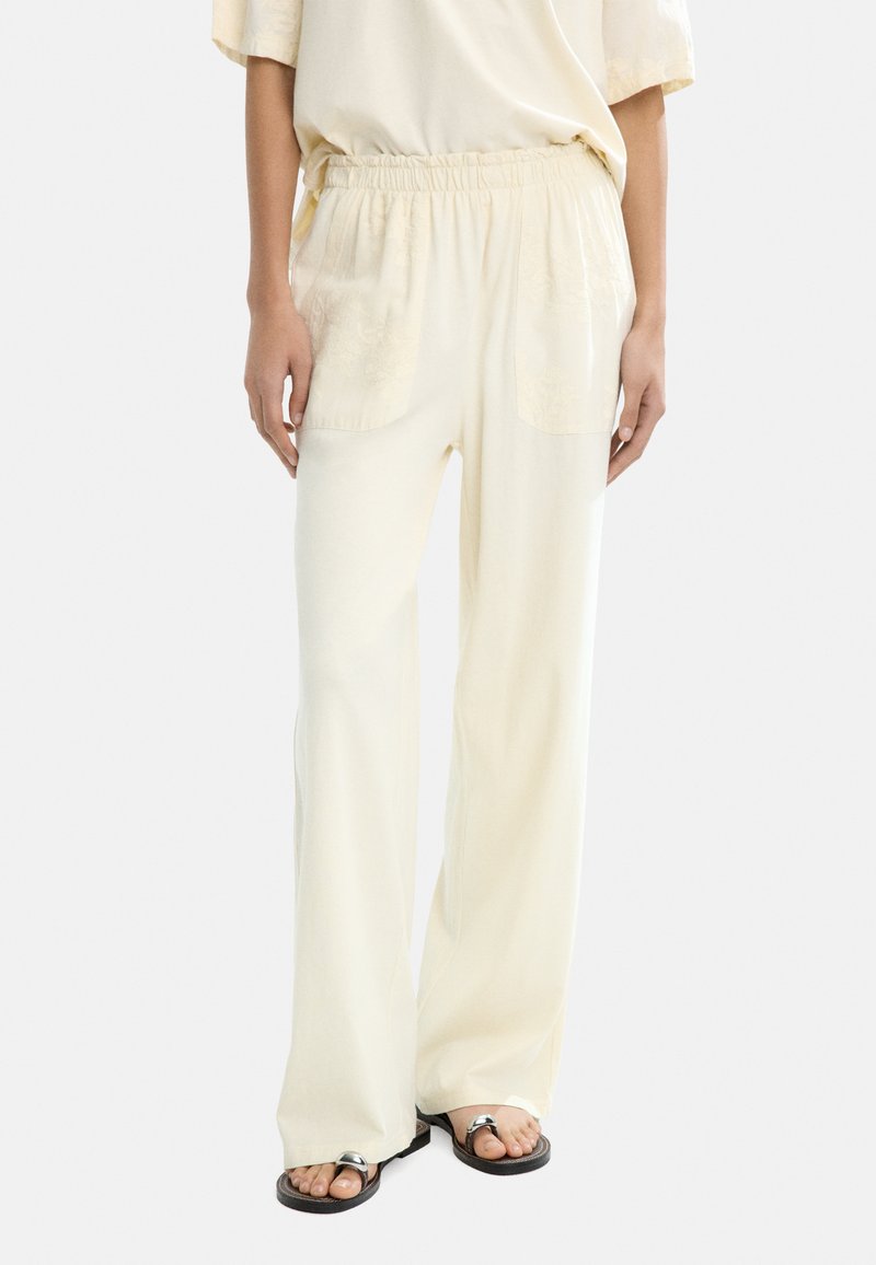 Jasnożółte szerokie spodnie z miękkiego materiału z elastyczną talią i dwiema przednimi kieszeniami, ozdobione subtelnym haftem w kwiaty.