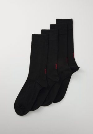 Cinq paires de chaussettes noires en coton, avec une texture lisse et un bord côtelé, ornées d'un petit logo rouge sur le côté de chaque chaussette.