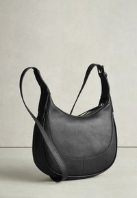 Černá kožená kabelka přes rameno s kulatým tvarem, strukturovaným povrchem a dlouhým nastavitelným popruhem. Má zipové zavírání a jemné detaily švů.