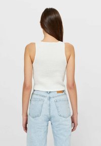 Witte mouwloze top met een gestructureerd, geplooid ontwerp, gecombineerd met high-waisted lichtblauwe jeans met een patch en klassieke zakken.