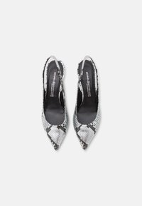 Zapatos de tacón slingback de punta fina en piel sintética de serpiente negra y plateada, que presentan un patrón texturizado y correas delgadas en el tobillo. Forro interior oscuro.