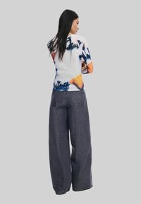 Langsleeve top met een kleurrijk abstract patroon; zacht materiaal. Gepaarde met losse, hoge taille donkergrijze jeans, met voorzakken.