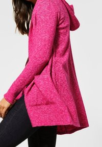 Langärmeliger Hoodie in lebhaftem Pink mit lockerem Schnitt, zwei Fronttaschen und längerem Saum hinten. Hergestellt aus einem weichen, strukturierten Stoff.