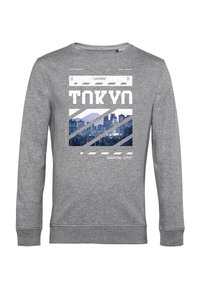 Felpa grigia con una stampa grafica che presenta il testo "TOKYO" e lo skyline della città, accentuata da strisce diagonali e silhouette di montagne.