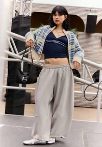 Pletiva kardigan s plavim, zelenim i krem kariranim uzorkom; tamnoplavi crop top; sivi široki hlače; crna torba s logom; srebrni slip-on cipele.