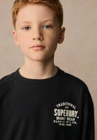 Sweatshirt negru cu guler cu rigle și un logo imprimat alb, purtat de un copil cu păr scurt blond și pistrui ăi ușori.
