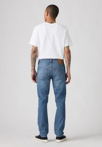 Blå denim jeans med rett snitt, to baklommer og en brun lær-patch på livlinjen, kombinert med en enkel hvit t-skjorte.