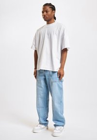 Hvid oversized bomulds t-shirt båret med lyseblå løse jeans. Outfit'et bliver fuldendt med hvide sneakers med teksturerede detaljer.