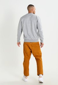 Sweatshirt gris avec un col rond classique, et pantalon orange à coupe décontractée, tous deux en tissu en coton mélangé texturé. Baskets blanches.