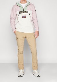 Lättvikts överdragströja i rosa och mintgrönt, med en framficka och logotypdetalj, ihop med beige cargo-byxor och vita sneakers.
