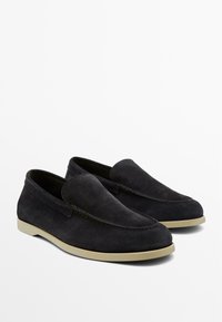 Sorte loafers i ruskind med beige gummisåler, runde tæer og synlige sømme langs de øverste kanter, vist side om side.