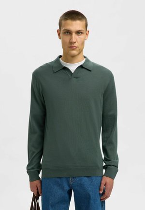 Polo-shirt vert à manches longues avec un col plat et un décolleté en V, fabriqué à partir d'un matériau doux. Associé à un jean en denim bleu et un sac brun.
