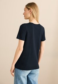 T-shirt bleu marine à manches courtes en coton, avec un col rond et une texture douce, associé à un jean large bleu clair.