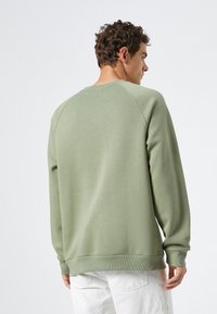 Sudadera verde con cuello redondo y mangas raglán, hecha de un material suave. Presenta puños y dobladillo acanalados, textura lisa.