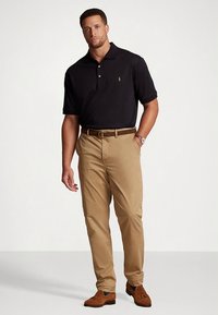 Μαύρο πόλο μπλουζάκι με τρία κουμπιά, χακί παντελόνι chinos, καφέ ζώνη και καφέ loafers. Λεπτό ύφασμα, εφαρμοστή γραμμή και μινιμαλιστική λεπτομέρεια με λογότυπο.