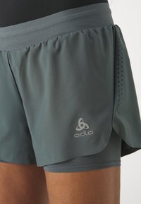 Los pantalones cortos deportivos grises presentan un diseño de capas con una capa interior ajustada. La tela es suave con detalles perforados y un logo en el lateral.
