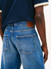 Sinine teksapüks, sirge lõikega, millel on kaks tagumist taskut ja pruun nahkänka, millel on kiri "TOMMY JEANS". Sile tekstuur, vabaaja disain.