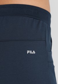 Marineblå, stretchiga joggerbyxor med ribbad midjeresår och sidofickor; har en vit Fila-logotyp nära höftområdet.