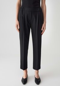 I pantaloni neri su misura presentano un tessuto liscio, una vita alta e delle leggere pieghe. Le gambe sono affusolate con una lunghezza cropped. Design semplice.