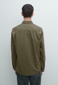Camicia abbottonata verde oliva con colletto, maniche lunghe e orlo curvo. Il tessuto sembra liscio con una leggera lucentezza.