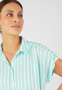 Lichtgewicht button-up shirt in aqua en witte verticale strepen. Bevat een klassieke kraag en opgerolde korte mouwen. Zachte stoftextuur.