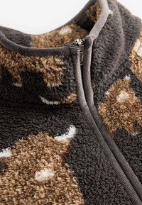 Fleecejas met grijze biezen, bruin-wit camouflagepatroon en een zilveren rits die gedeeltelijk gesloten is bij de voorkraag.