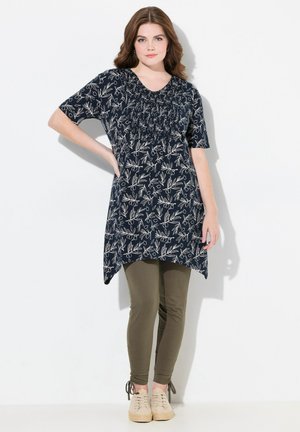 Tunic navy con motivo floreale bianco, scollatura arricciata, abbinata a leggings oliva e scarpe beige. Tessuto morbido, vestibilità comoda, maniche corte.