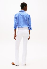 Camisa de rayas azul y blanca de manga larga, con el cuello y los puños remangados, combinada con pantalones vaqueros blancos acampanados y zapatos marrones. Diseño limpio y minimalista.