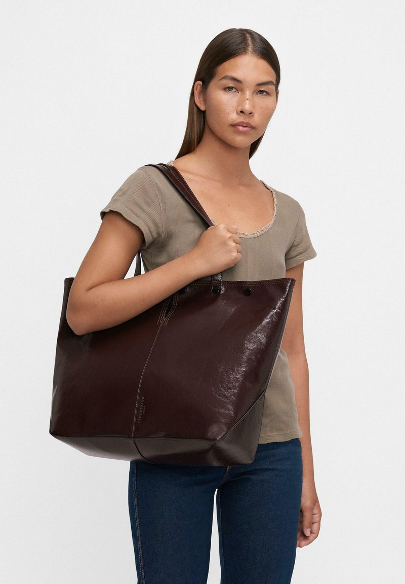 Duża brązowa skórzana torba tote o gładkiej fakturze, z wyraźnym kształtem i dwiema górnymi rączkami. Idealna do codziennego użytku.