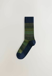 Chaussette marine unique avec un motif pied-de-poule horizontal vert et jaune sur la jambe et le pied, pointe et bord-côte unis marine, posée à plat sur une surface blanche.