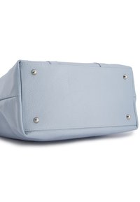 Lichtblauwe leren tas met een gestructureerd oppervlak, vierkante vorm en zilveren metalen voeten voor stabiliteit aan de basis. Platte, gestikte details aanwezig.