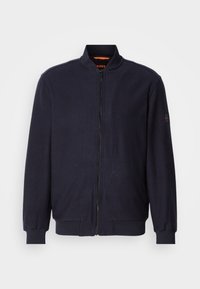 Veste polaire bleu marine zippée avec col, poignets et ourlet côtelés, dotée d'un petit patch logo sur la manche gauche.