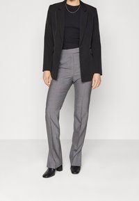 Czarna marynarka o dopasowanym kroju z klapami, zestawiona z szarymi spodniami w kratę o wysokim stanie. Całość dopełniają czarne botki sięgające do kostek.