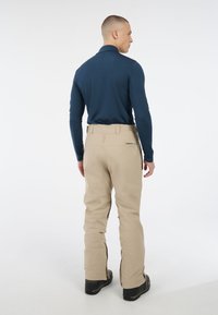 Beige waterdichte broek met ritsen bij de enkels, gecombineerd met een aansluitend donkerblauw longsleeve shirt. Glad textuur en op maat gemaakte pasvorm.