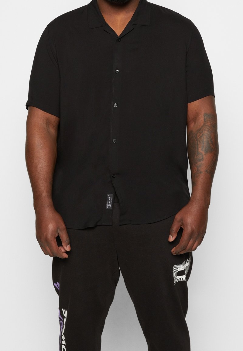 Zwart overhemd met korte mouwen van gladde stof, voorzien van een notch-kraag en een enkele pocket op de linkerkant van de borst.