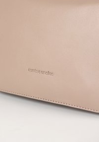 Beige Lederbörse mit eingeprägtem "aunts & uncles"-Logo, glatter Textur und präziser Naht entlang der Kanten.