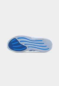 Semelle d'une chaussure de sport gris clair et bleu avec des motifs de traction texturés et des lignes de traction bleues incurvées.
