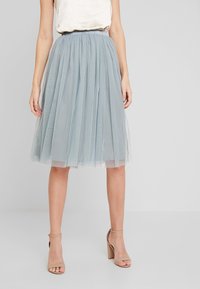Gonna in tulle azzurro chiaro con plissettature, cintura elastica e design a strati, caratterizzata da una texture leggera e trasparente. Abbinata a sandali con tacco.