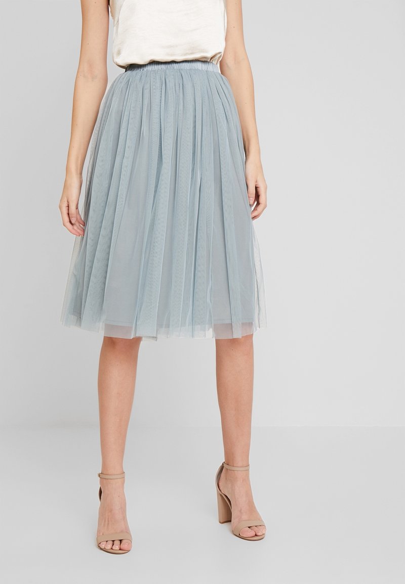 Gonna in tulle azzurro chiaro con plissettature, cintura elastica e design a strati, caratterizzata da una texture leggera e trasparente. Abbinata a sandali con tacco.