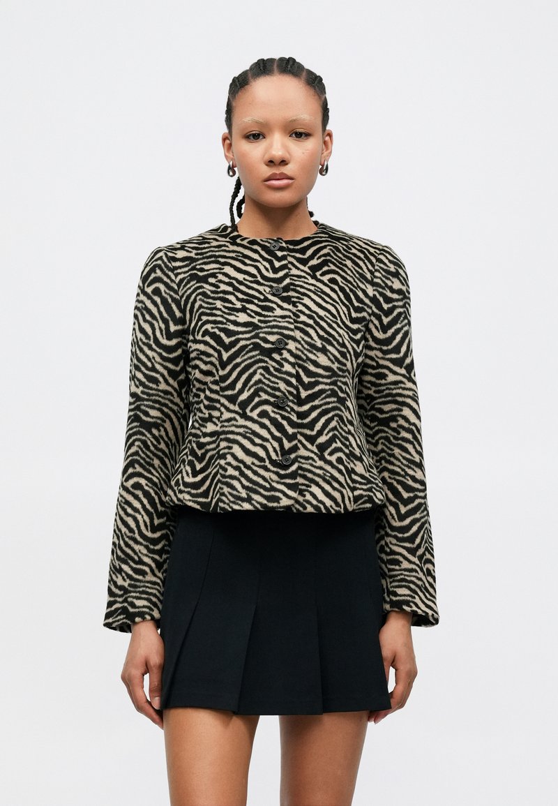 Chaqueta con estampado de cebra en tejido beige y negro, con mangas largas y cuello redondo, que cuenta con seis botones en la parte frontal.
