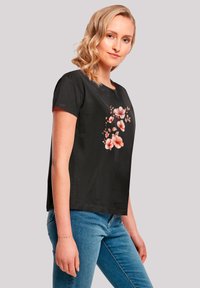 Black short-sleeve t-shirt featuring a floral print in soft pink and white. The fabric appears smooth, with a relaxed fit and simple neckline.