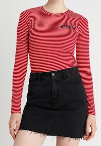 Röd och vit randig långärmad tröja med en svart logotyp, tillsammans med en svart denim mini kjol med fransad nederkant och framfickor.