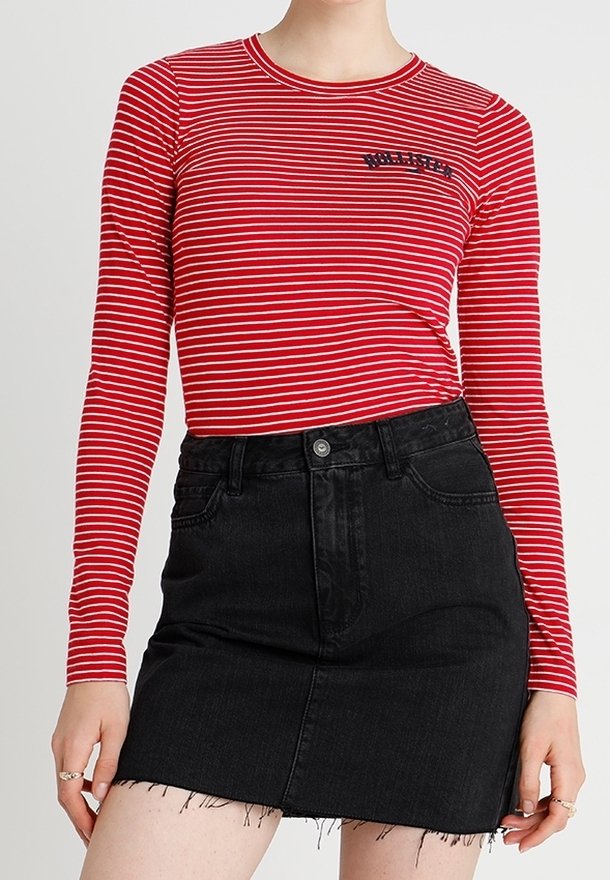 Röd och vit randig långärmad tröja med en svart logotyp, tillsammans med en svart denim mini kjol med fransad nederkant och framfickor.