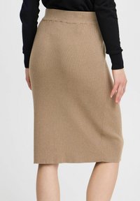 Jupe beige côtelée de longueur genou avec une taille ajustée, présentant un tissu texturé et un détail de fente sur le côté.