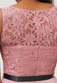 Tissu en dentelle rose avec un motif floral, superposé sur la partie supérieure ; accents en sequins ; ceinture en satin noir ; fermeture éclair dissimulée à l'arrière.