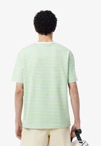 Camiseta de algodón a rayas verde claro, con mangas cortas y cuello redondo. Las rayas alternan entre tonos más oscuros y más claros.